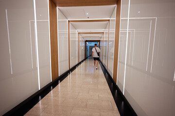 Modern corridor with seamless lighting and lone traveler walking into a bright space