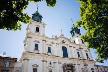 Elegant Church of the Holy Cross building surrounded by green trees under a bright blue sky. Warsaw, Poland.