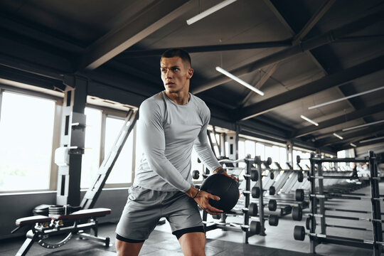 Horizontal photo of a fit male athlete training with a medicine ball at the gym. The strong young man is performing a strength exercise using the fitness ball.  - Powered by Adobe