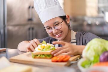 Smiling Young Female Chef Preparing a Sandwich in a Professional Kitchen