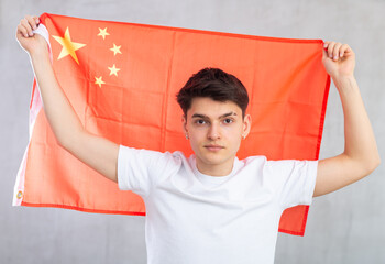 Young focused guy posing with big flag of China in his hands in studio