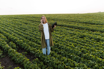 Modern agribusiness. Happy female farmer with digital tablet, talks on smartphone after examine and...