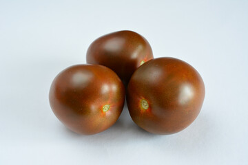 Three ripe black tomatoes on a white surface close up