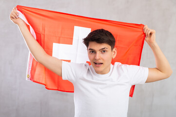 Middle-aged positive man in casual clothes holds unfurled flag of Switzerland in hands raised above...