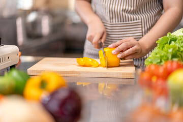 Chef Slicing Yellow Bell Pepper on Wooden Cutting Board in Professional Kitchen