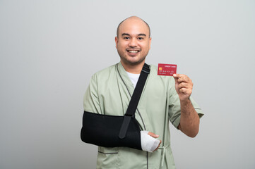 An Asian man in a hospital gown smiles gently at the camera with his arm bandaged and bandaged,...