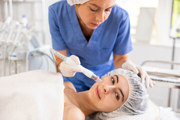 Young female cosmetologist performs facial cleansing procedure on young female client