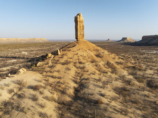 Aerial view of the stark, sun-baked landscape where a monolithic rock pillar rises dramatically against a clear blue sky, Damaraland, Kunene region, Namibia.