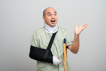 Asian man in hospital gown smiles gently at camera with arm bandages and bandages and crutches, posing to show resilience and positive attitude during recovery.