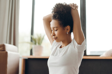 Young African American woman athlete closing eyes, stretching arms on yoga mat at home