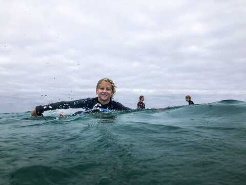 Young male surfer in ocean paddling on boogie board with two surfers sitting on boards in background