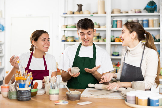 Two young women and young man sculpt pottery in workshop - Powered by Adobe