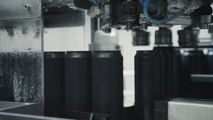 Aluminum cans traveling along a conveyor belt are passing beneath an automated sealing machine in a...
