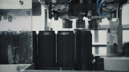Automated machinery processing black aluminum cans on a production line inside a beverage factory, representing industrial manufacturing and packaging processes