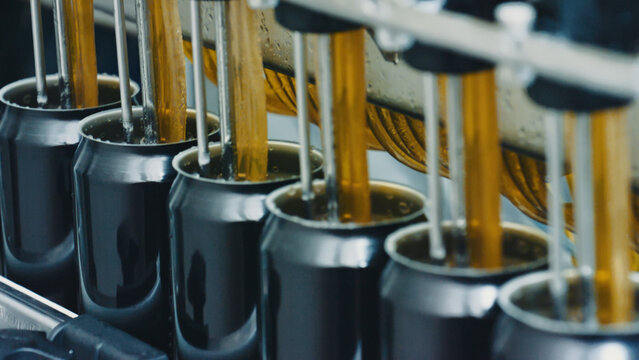 Automated machine pouring carbonated drink into aluminum cans on a production line in a modern beverage factory, representing industrial automation, efficiency, and mass production
