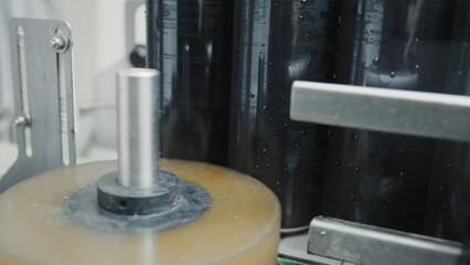 Automated labeling machine applying adhesive labels to wet aluminum cans on a conveyor belt in a beverage factory, ensuring product branding and identification