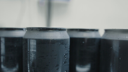 Freshly produced black aluminum cans with condensation droplets stand in a row on a conveyor belt...