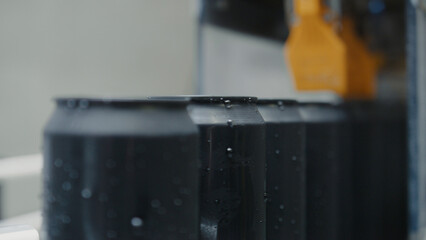 Freshly filled black aluminum cans with condensation droplets moving along a conveyor belt, being...