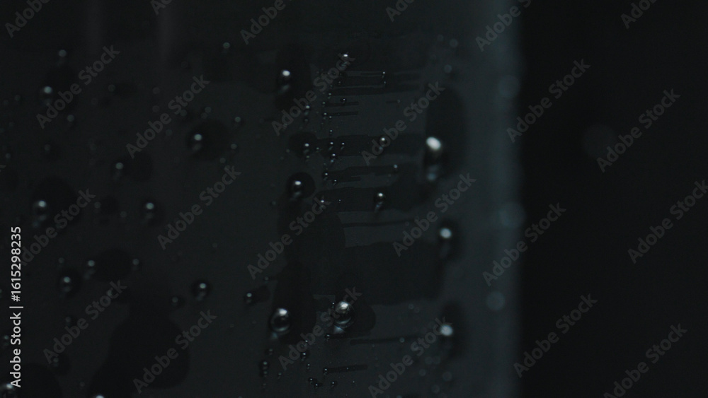 Poster close up of water droplets forming abstract patterns on a dark, reflective surface, creating a visua