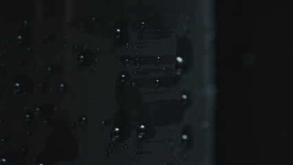 Close up of water droplets forming abstract patterns on a dark, reflective surface, creating a...