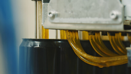 Automated industrial equipment filling black aluminum cans with a carbonated beverage on a...