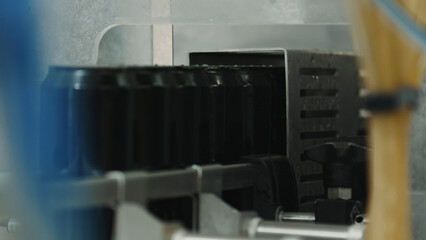 Many black aluminum cans are moving on a conveyor belt inside an industrial machine, during a production process, probably for beverage canning