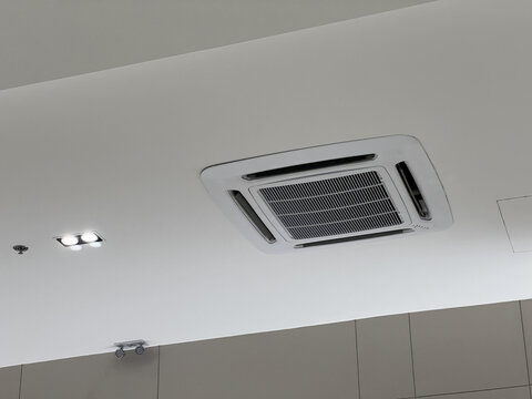 Modern white cassette air conditioner system on ceiling providing cool comfort. An indoor unit for ventilation, air conditioning, and climate control technology at home or office