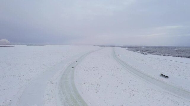 Aerial view of vehicles travelling on a snow-covered frozen river under a pale sky, contrasting the white expanse with the dark vehicles, Yakutsk, Sakha Republic, Russia.