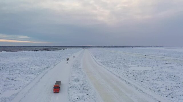 Yakutsk, Russia - 29 July 2025: Aerial view of vehicles traversing a snow-covered road amidst a vast, icy landscape under a cloudy sky, creating a stark contrast.