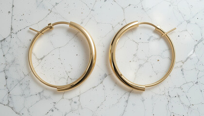 A pair of gold hoop earrings displayed on a white marble surface with subtle grey veining pattern design