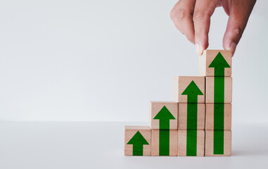 A concept of business growth and success. A hand builds a staircase of wooden blocks with upward arrows, symbolizing progress, increased sales, and profit. A strategy for development.