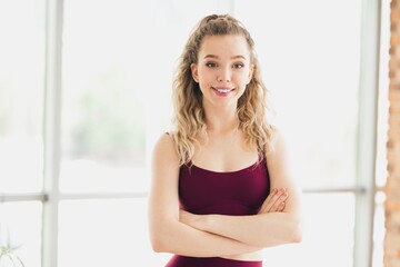 Attractive female athlete in red activewear confidently posing indoors in bright natural light for...