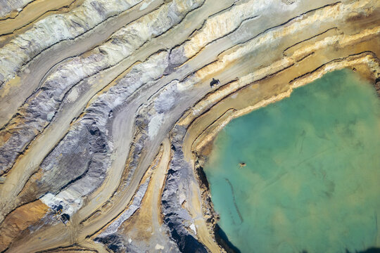 Aerial view of the striking contrast between the stepped terraces of the Erzberg mine and a vibrant turquoise lake, Eisenerz, Styria, Austria.