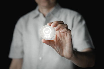 A person holds up a physical cube wooden displaying a prominent digital icon of a certified badge with a checkmark, symbolizing quality assurance, excellence, and a guarantee of high standards.