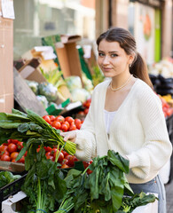 Young woman buyer choosing fresh spinach at vegetable market
