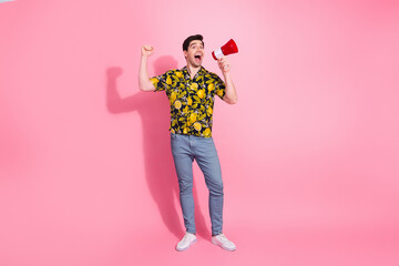 Cheerful young man in a vibrant shirt holding a megaphone and celebrating against a bright pink background