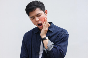 close up young asian man frown and use hand to massage on cheek after feeling pain or hurt from tmj...