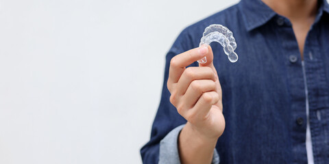 close up young man hand holding dental aligner retainer (invisible) on white background at dental clinic for beautiful teeth treatment course concept