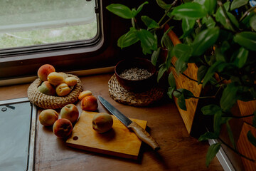 A wooden table with a cutting board, knife, and fresh peaches. A plant and a bowl of grains are...