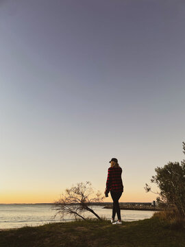 Silhouette of woman standing in front of coastal marina background at twilight
