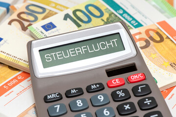 Ein Taschenrechner ist im Display beschriftet mit dem Wort Steuerflucht und liegt auf vielen Euro...