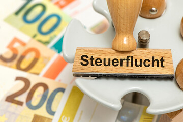 Ein Holzstempel ist beschriftet mit dem Aufdruck Steuerflucht über vielen Euro Banknoten