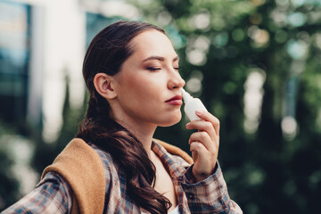 Young woman enjoys fresh outdoor air with nasal spray on an urban street during a pleasant autumn...