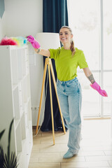 Young woman in bright casual clothing cleaning bookshelf at home during spring cleaning, enjoying a...