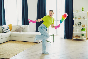 Energetic young woman dancing while cleaning her living room in casual stylish attire