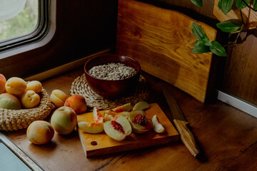 A wooden table with a cutting board, knife, and fresh peaches. A plant and a bowl of grains are...