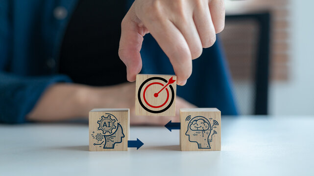 Hand arranging wooden blocks with AI and brain icons pointing to the target symbol, representing artificial intelligence, machine learning, digital transformation, and business goal achievement.