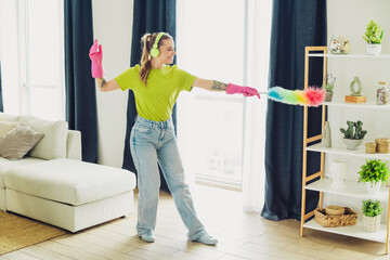 Young woman cleaning a cozy living room interior while listening to music and enjoying springtime...
