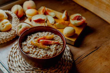 A bowl of sliced peaches and apples sits on a woven mat. Fresh peaches are scattered around, with a wooden spoon resting beside the bowl.