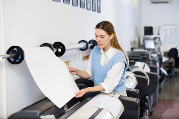 Woman working in publishing facility, loading large format paper in printer.